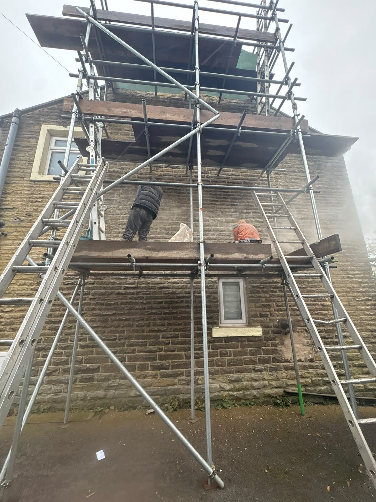 Roofers working from scaffolding on a gritstone terrace during roof repairs in East Lancashire