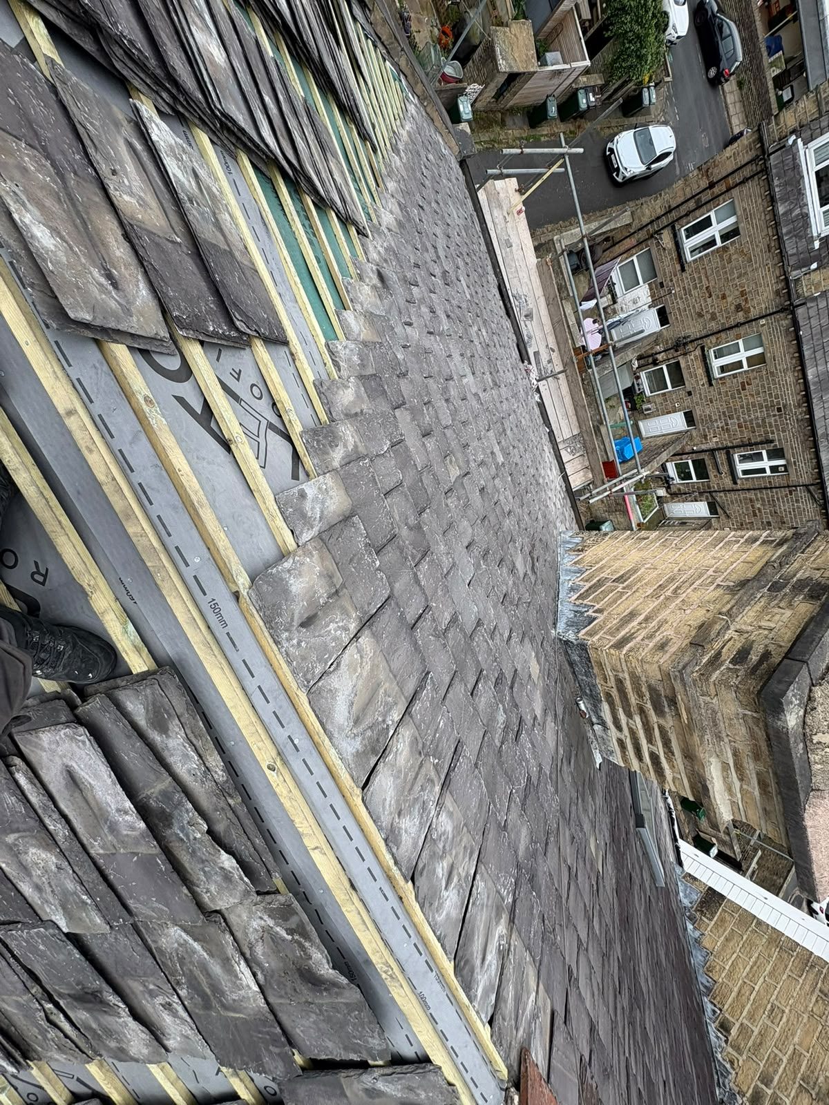 Reclaimed stone slates being re-laid over new membrane and battens during a re-roof on a terraced property
