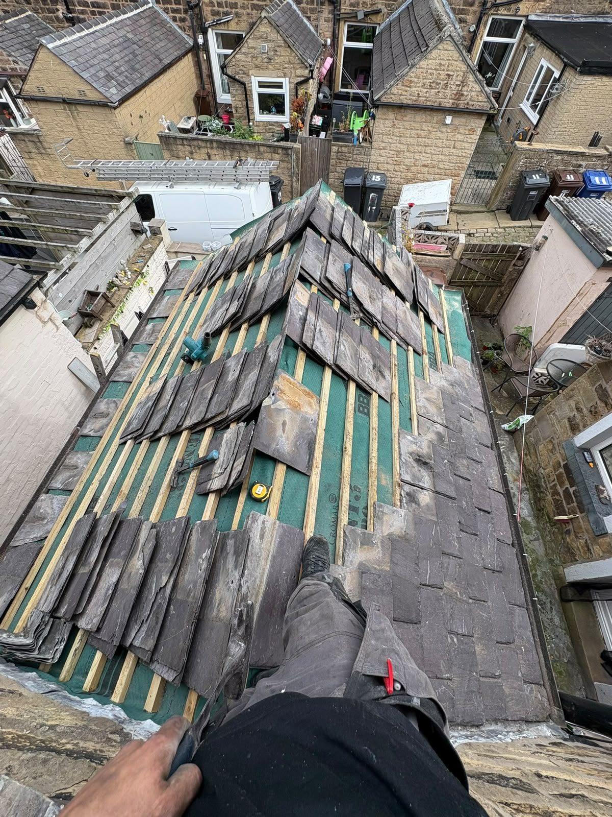 Reclaimed stone slates being re-laid over new membrane and battens on a terraced roof in East Lancashire