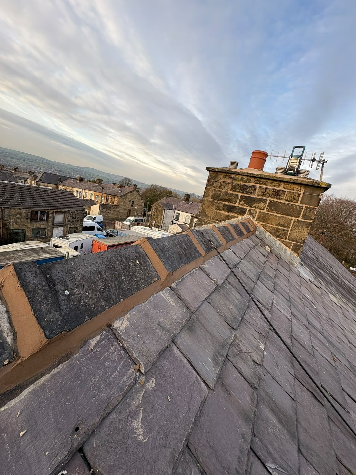 Repointed hip and ridge tiles beside a re-flashed stone chimney on a terraced roof
